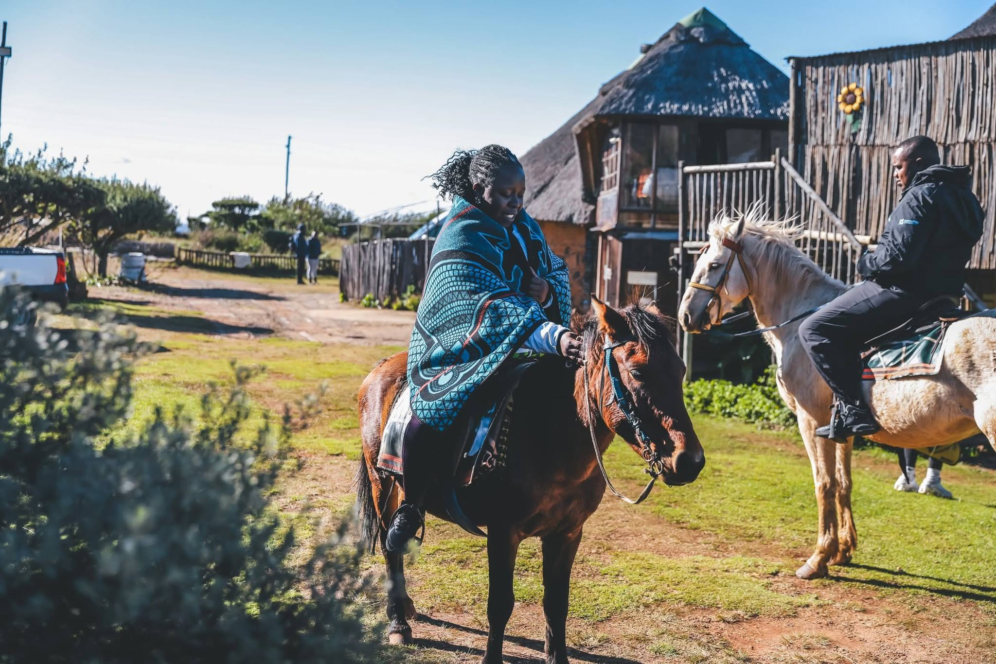 Visitors riding horses beside thatched buildings